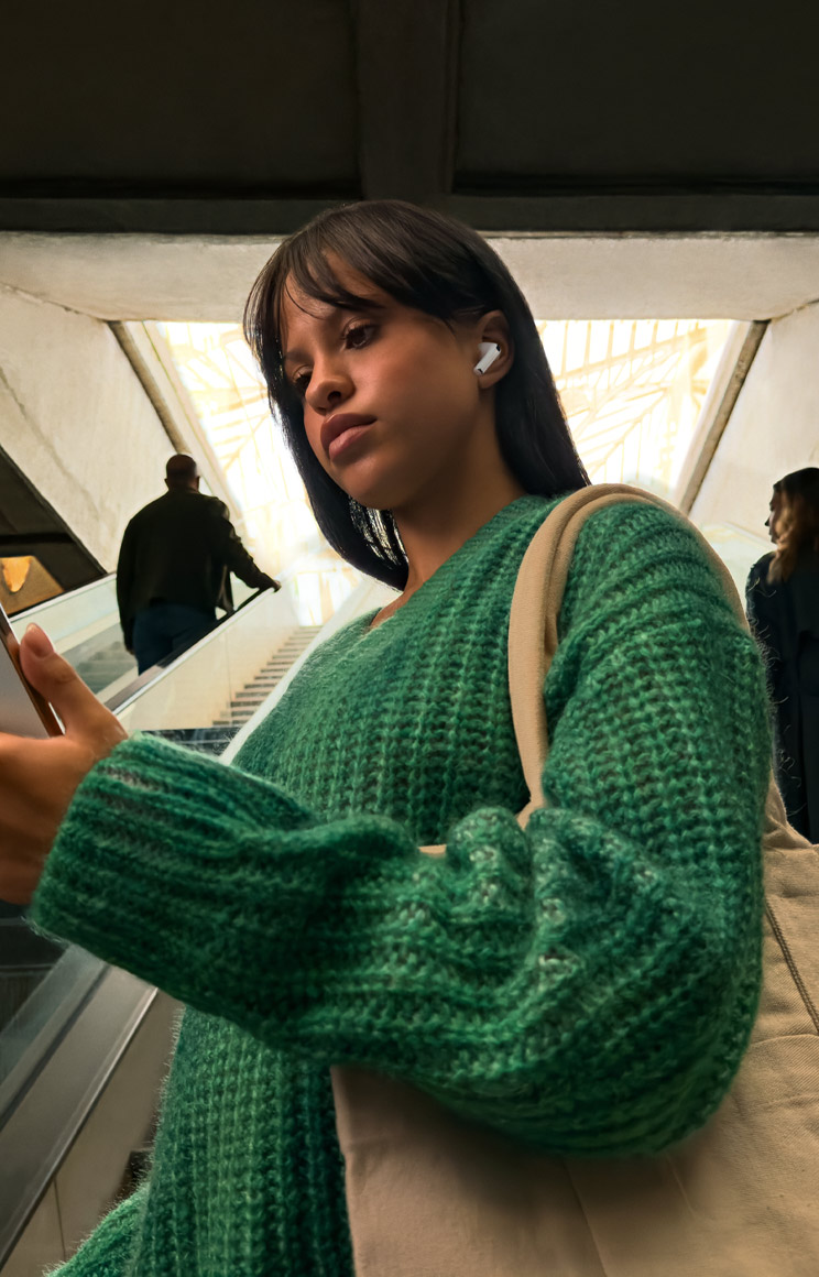 A person walking through a busy street wearing AirPods Pro 3